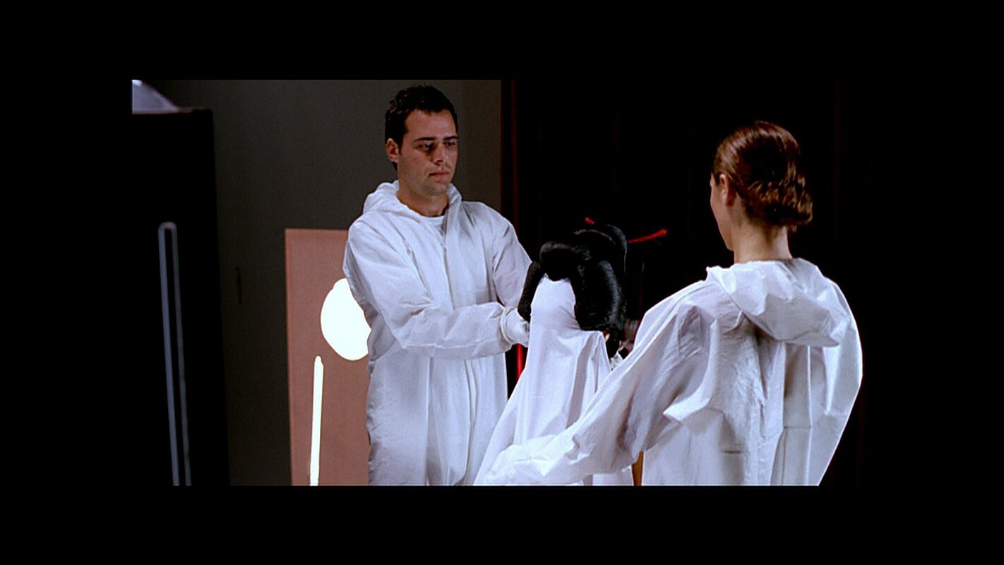 Screenshot aus dem Film: 2 Personen in weißer Kleidung mit einer ebenfalls weiß gekleideten Modebüste