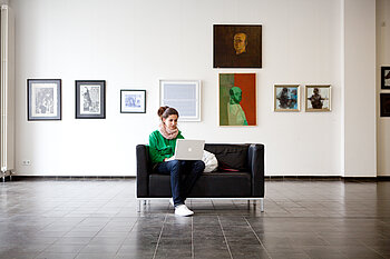 Studentin mit Laptop auf einem Sofa im Foyer von Gebäude A auf dem Campus Wilhelminenhof