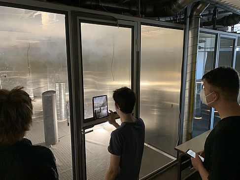 3 Studierende stehen vor einer Glaswand und beobachten Rauch in einem Labor © HTW Berlin/O ja!