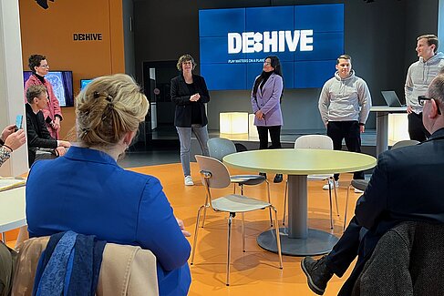Franziska Giffey und Oliver Igel sehen sich eine Präsentation an, im Hintergrund eine Leinwand mit dem Schriftzug DE:HIVE
