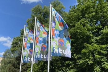 Fahnen am Campus Treskowallee. Das bunte, grafisch Motiv zeigt unterschiedliche Menschen. © HTW Berlin/Anja Schuster